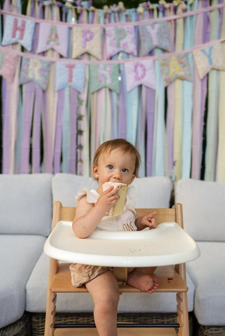 A one-year-old in a high chair eating birthday cake