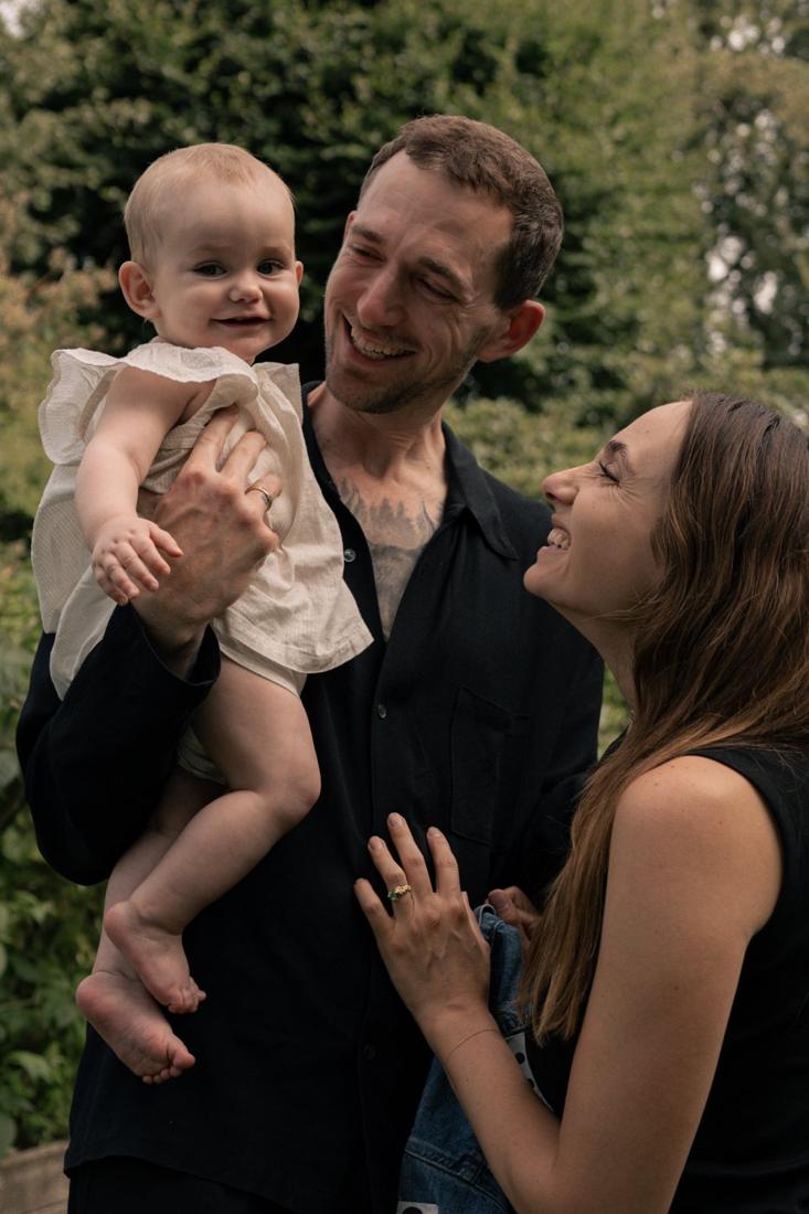 Dad lifting his smiling baby girl while mom laughs beside them in a garden