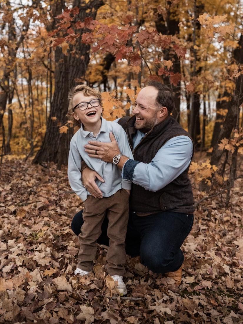 A dad and his little boy laughing together in the fall leaves