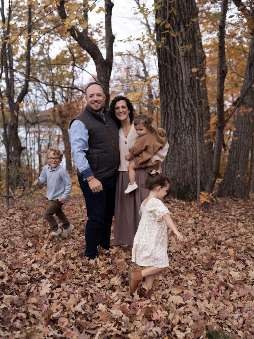A whole family together in the fall leaves, the kids running and twirling around mom and dad