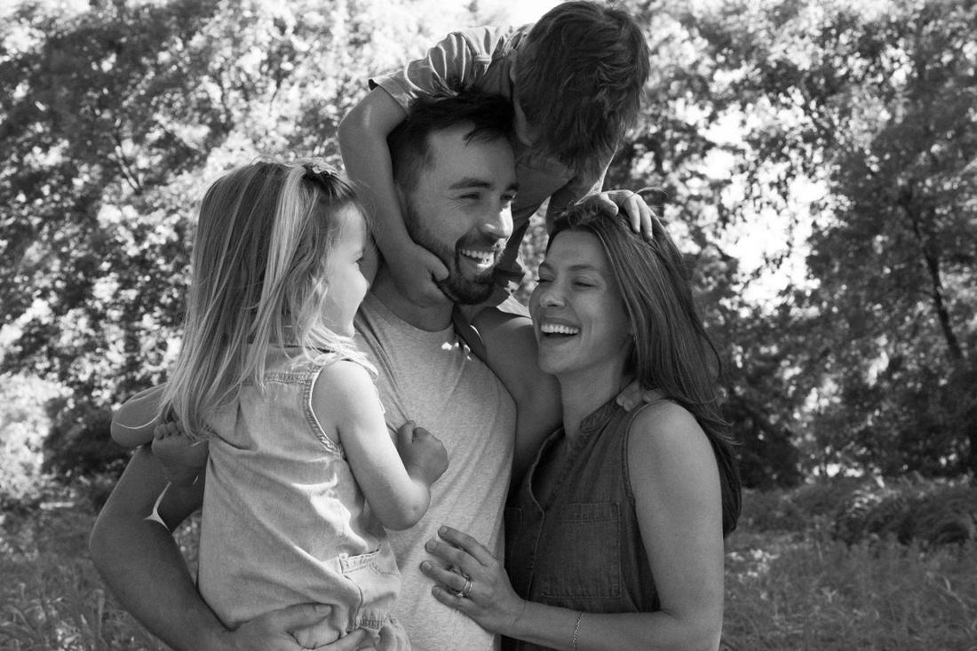 Dad laughing with his son on his shoulders, his daughter in his arms and his wife beside him, in black and white