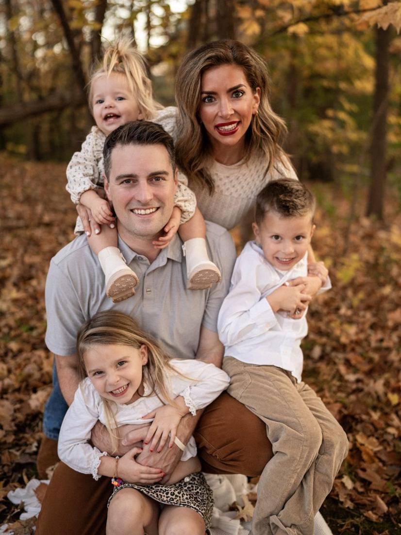A mom and dad in the fall leaves with their three kids piled on