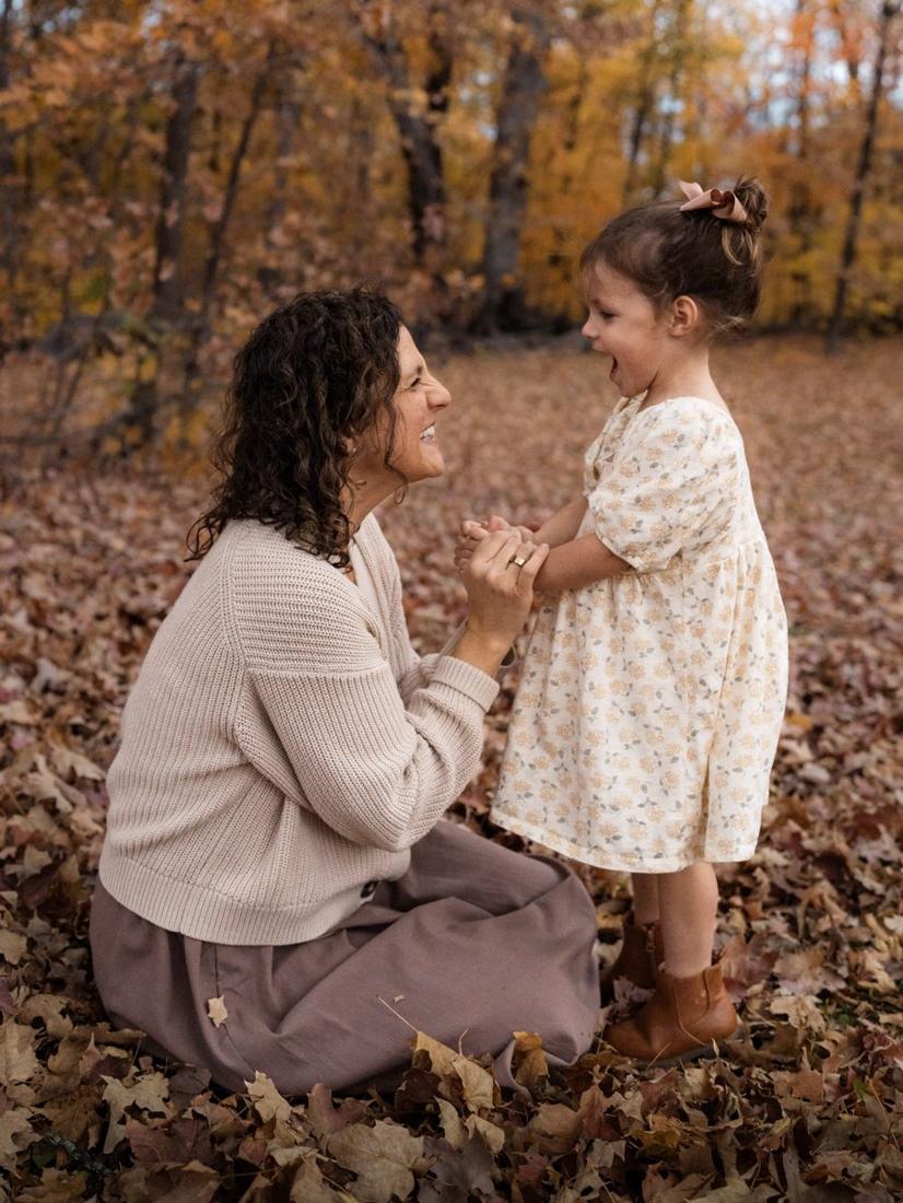 A curly-haired mom holding her daughter’s hands