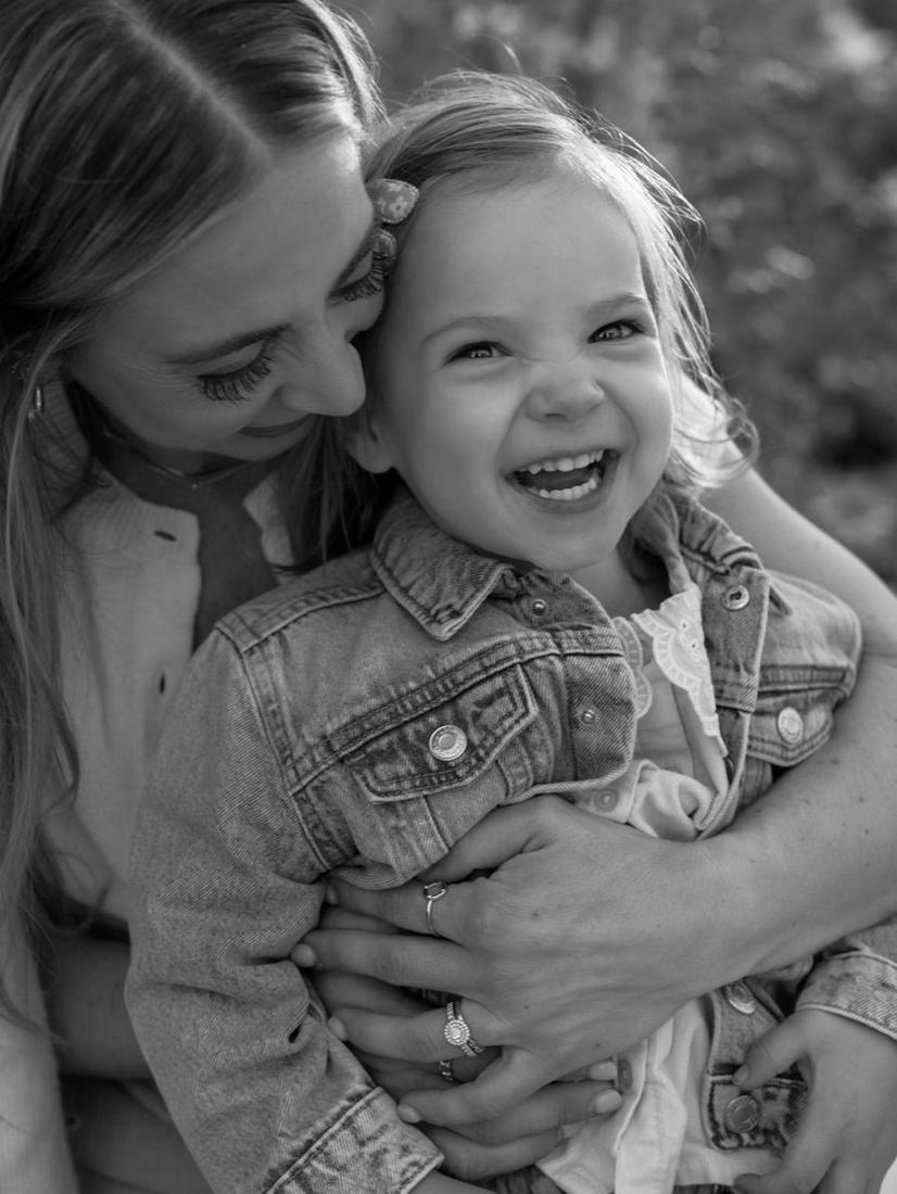 A mom squeezing her laughing toddler tight, in black and white