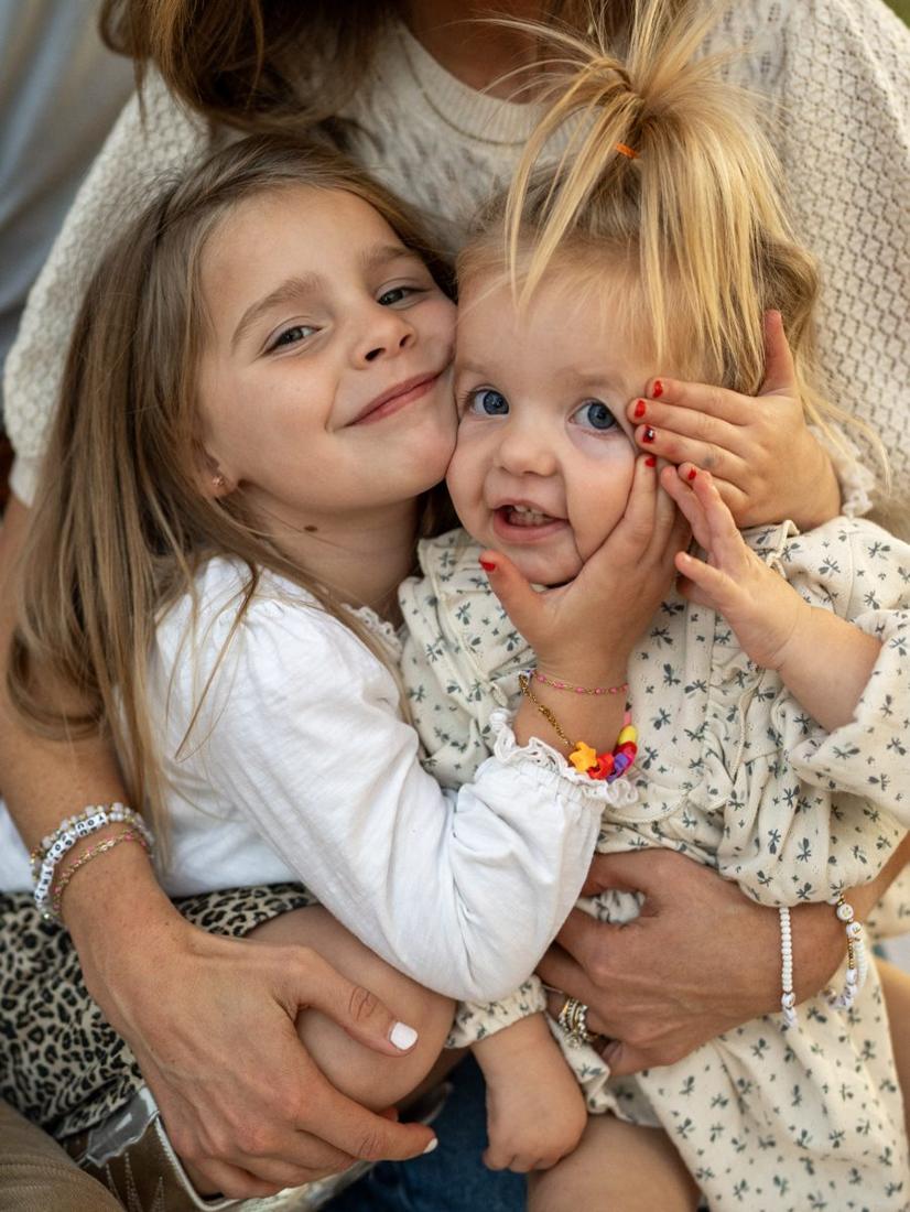Two sisters squeezed cheek to cheek in their mom’s arms