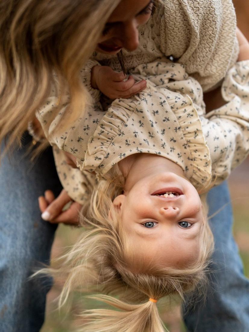 A little girl hanging upside down, laughing, held by her mom
